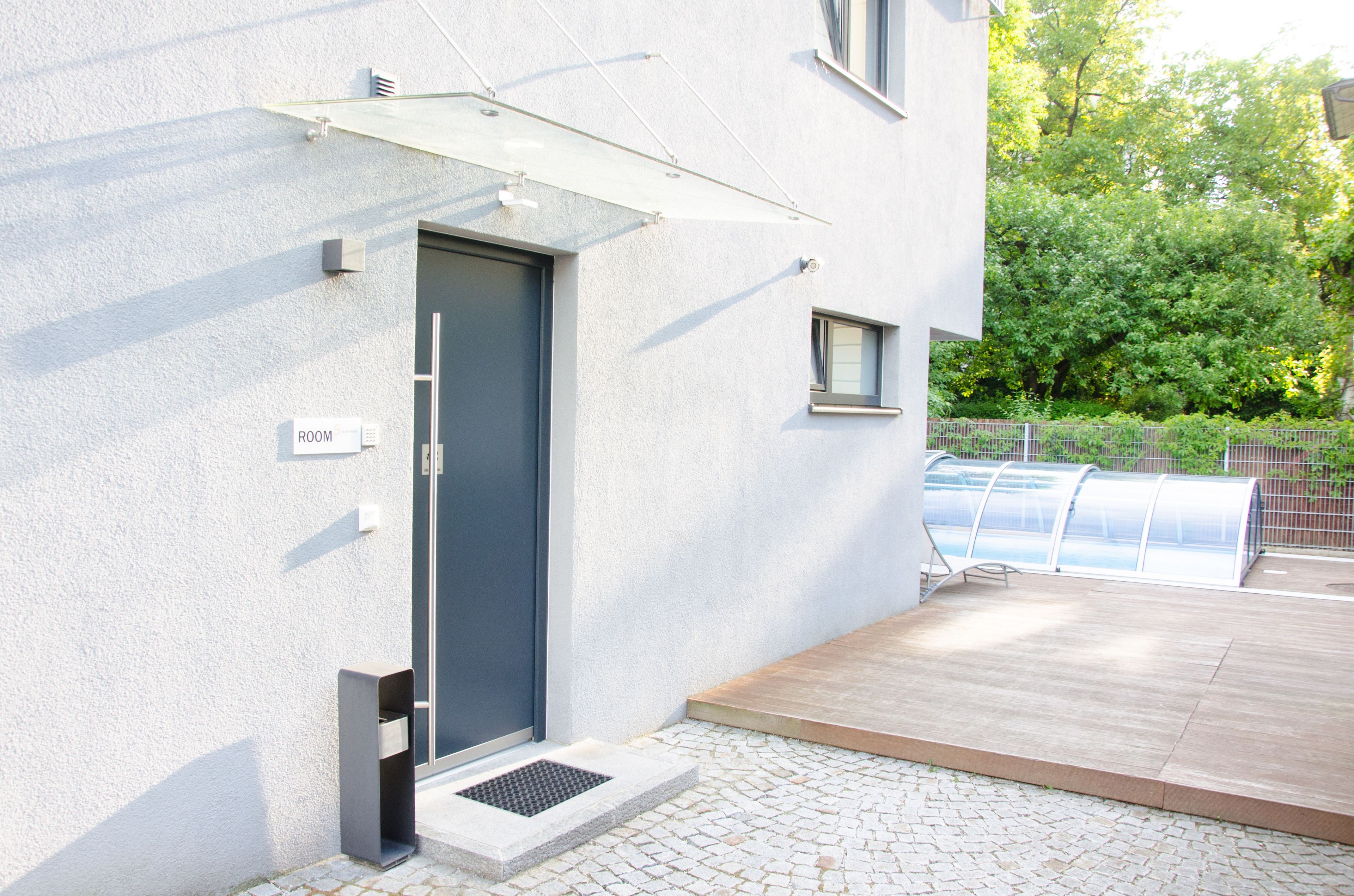 Un edificio moderno con una puerta gris, un ventanal pequeño y un toldo metálico sobre un área de patio.