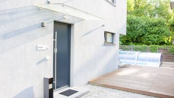 Un edificio moderno con una puerta gris, un ventanal pequeño y un toldo metálico sobre un área de patio.