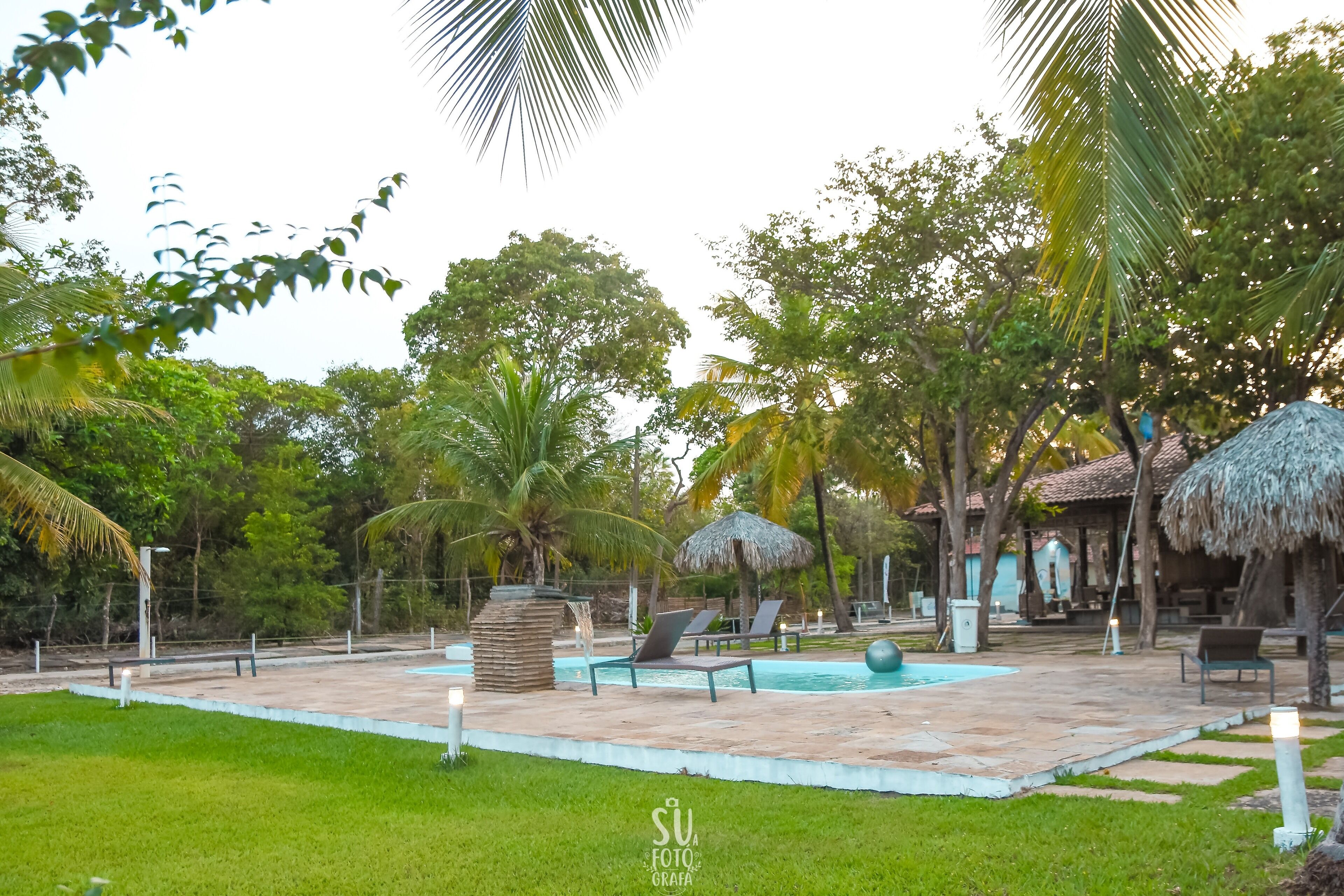 A pool area with lounge chairs, a thatched-roof structure, and a stone water feature.