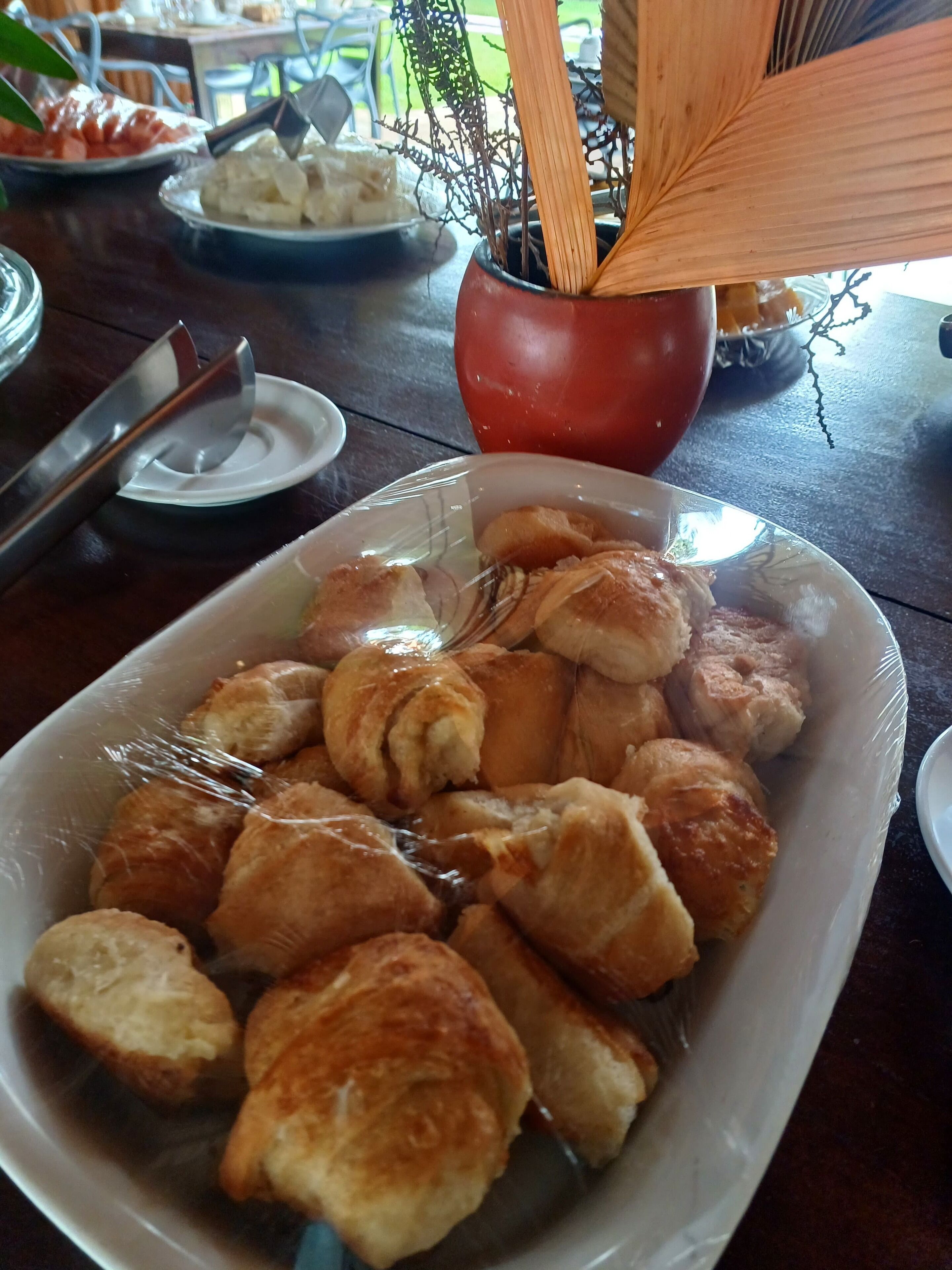 A table with a plate of croissants and a red bowl with a spoon.