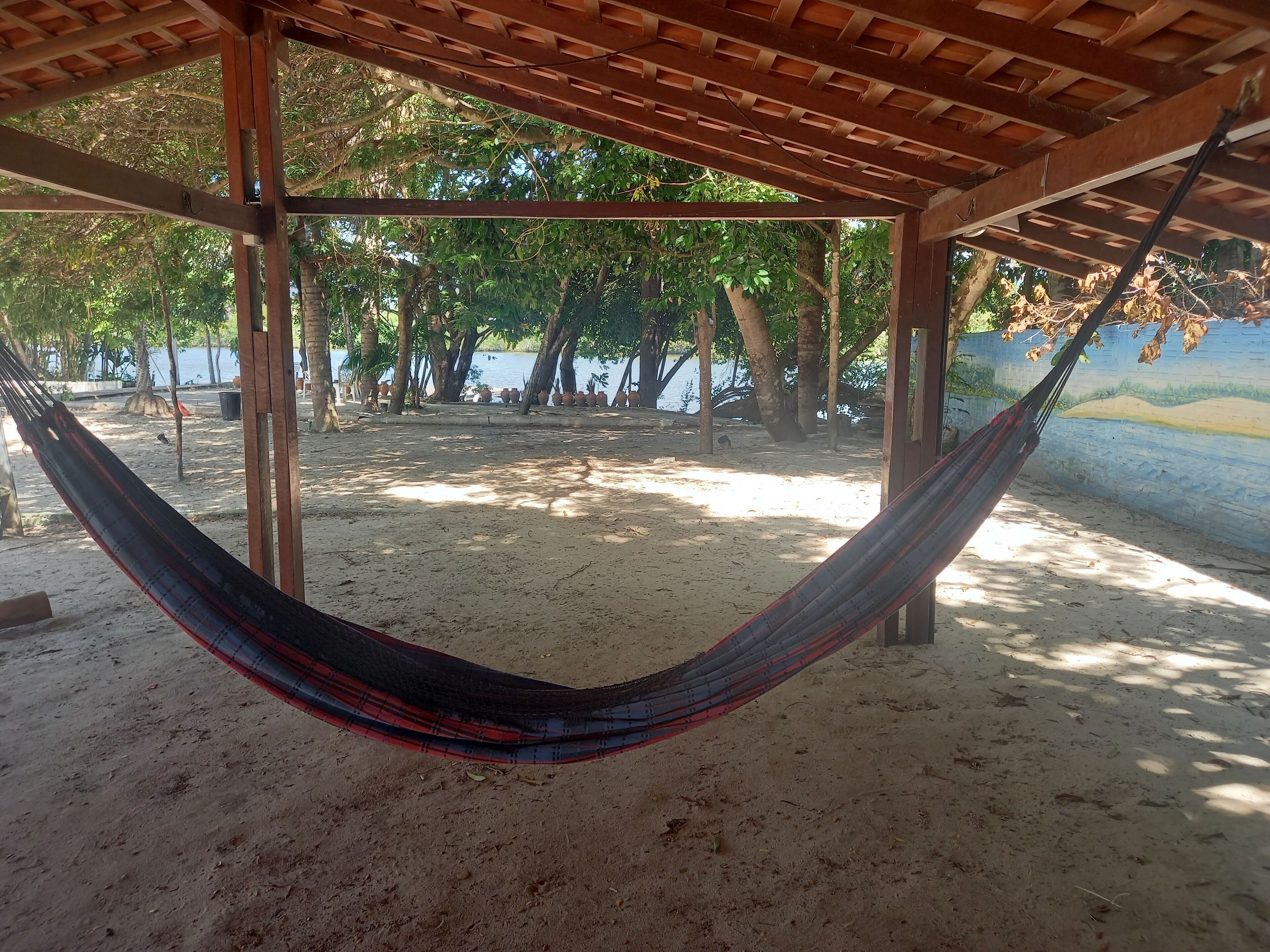 Una hamaca bajo una pérgola de madera con vista a una playa y árboles.