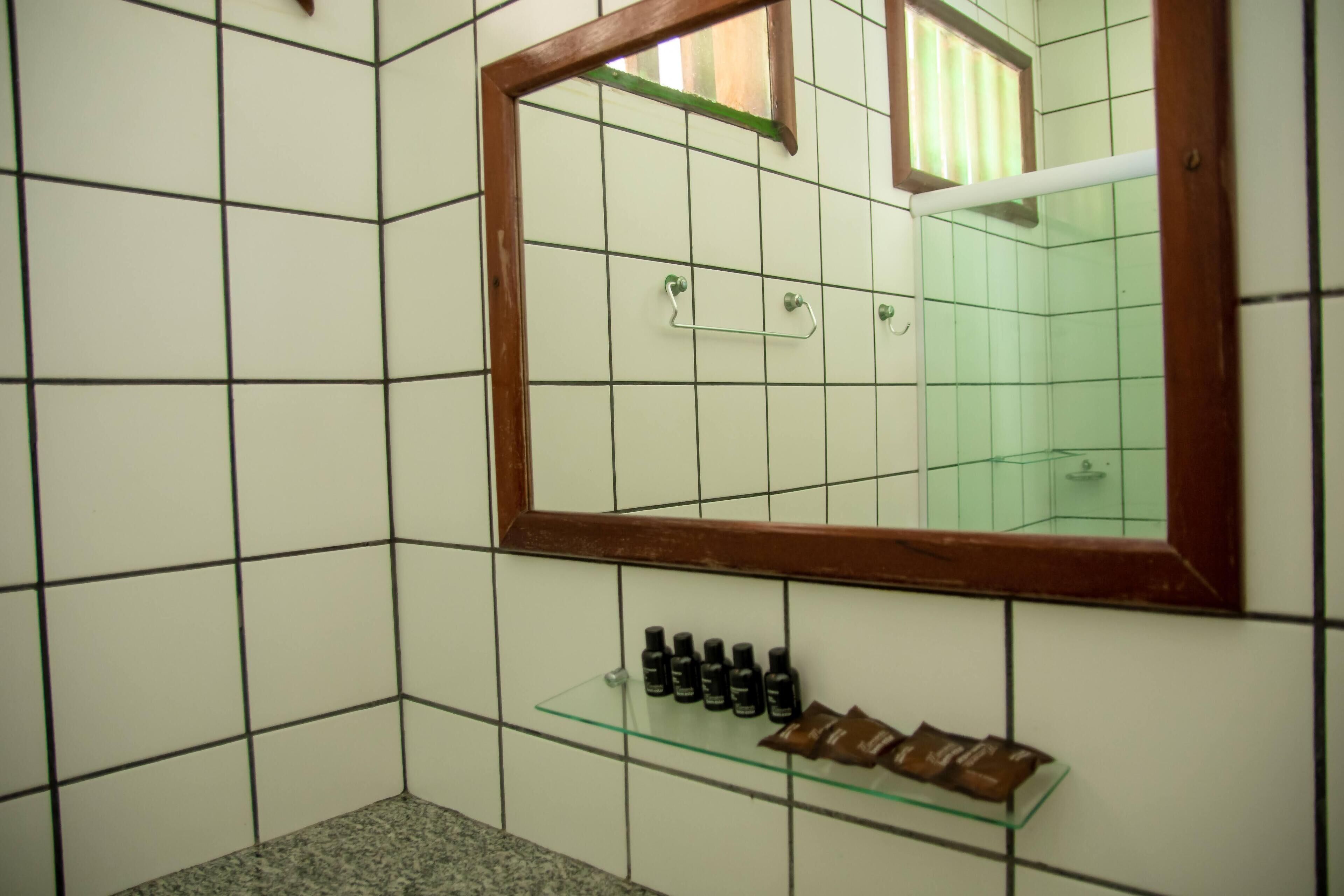 Et badeværelse med hvide flisevægge, et spejl med træramme og en hylde med toiletartikler.
