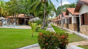A row of white buildings with red-tiled roofs, a palm tree, and a well-maintained lawn. - Orla Náutica Pousada (Barreirinhas)