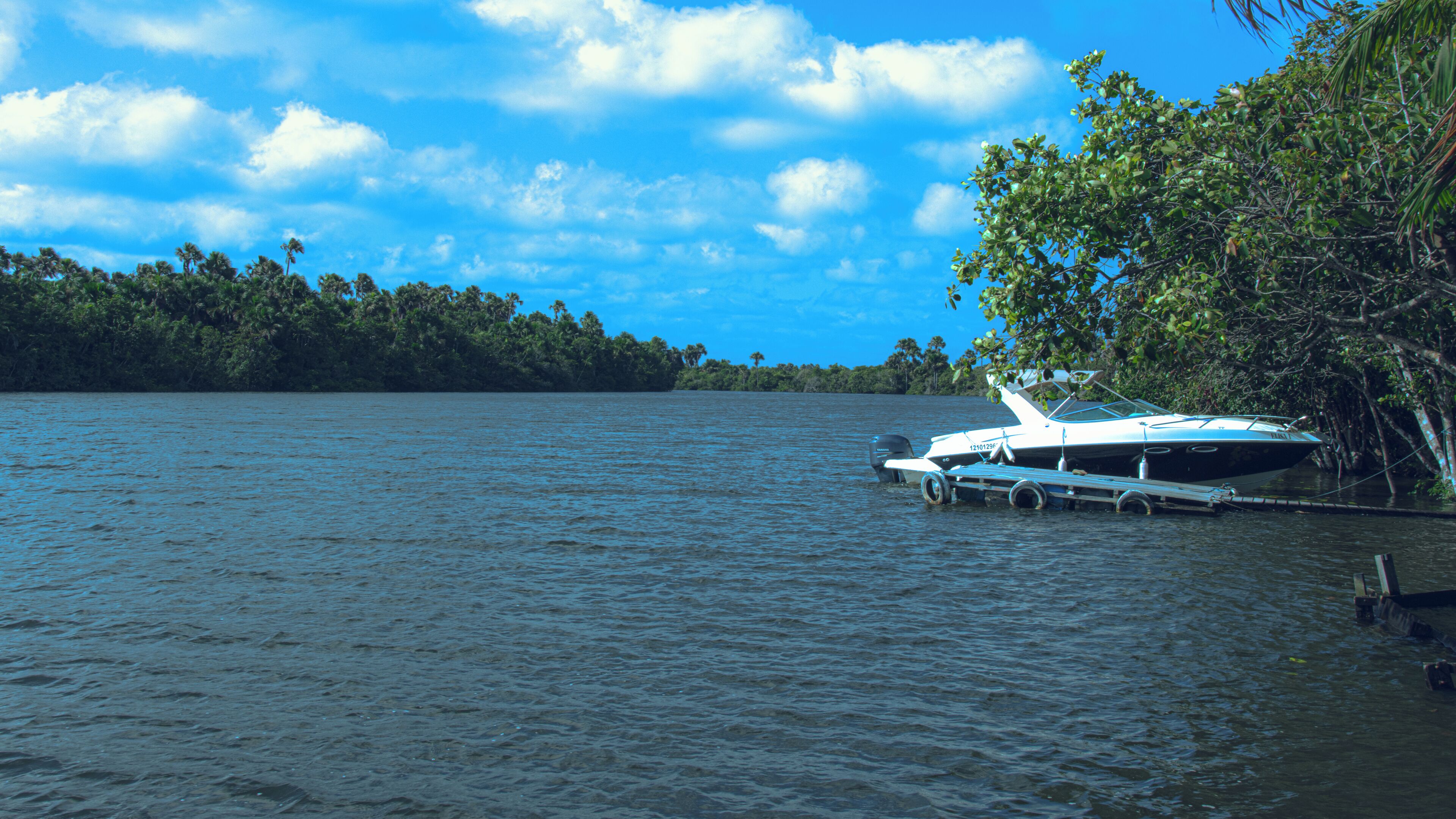 A boat docked at a pier with a forested shoreline in the background.