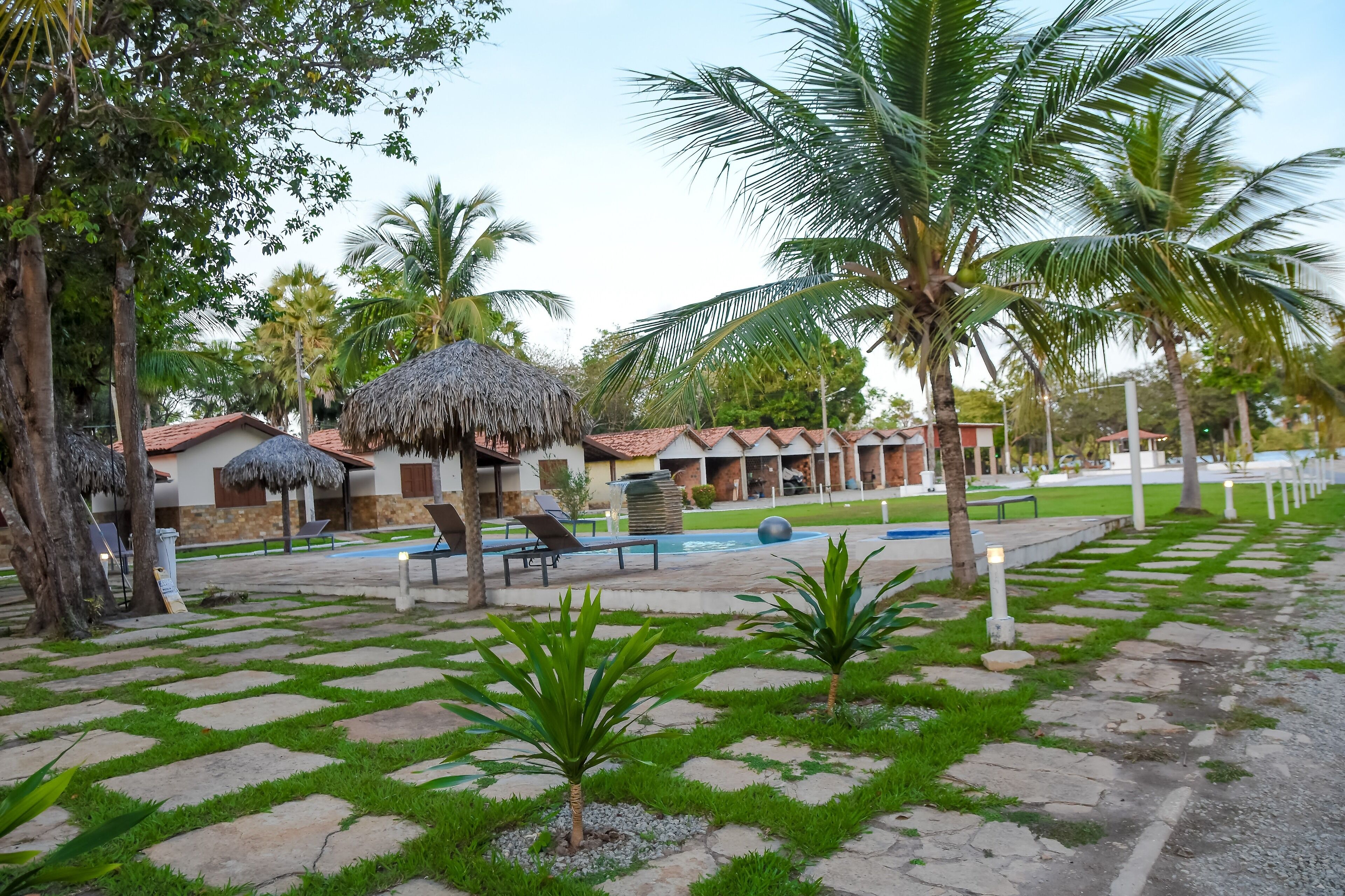 Un complexe hôtelier doté de bungalows aux toits de chaume, d’une piscine et d’un jardin bien entretenu, agrémenté de palmiers et d’un sentier en pierre.