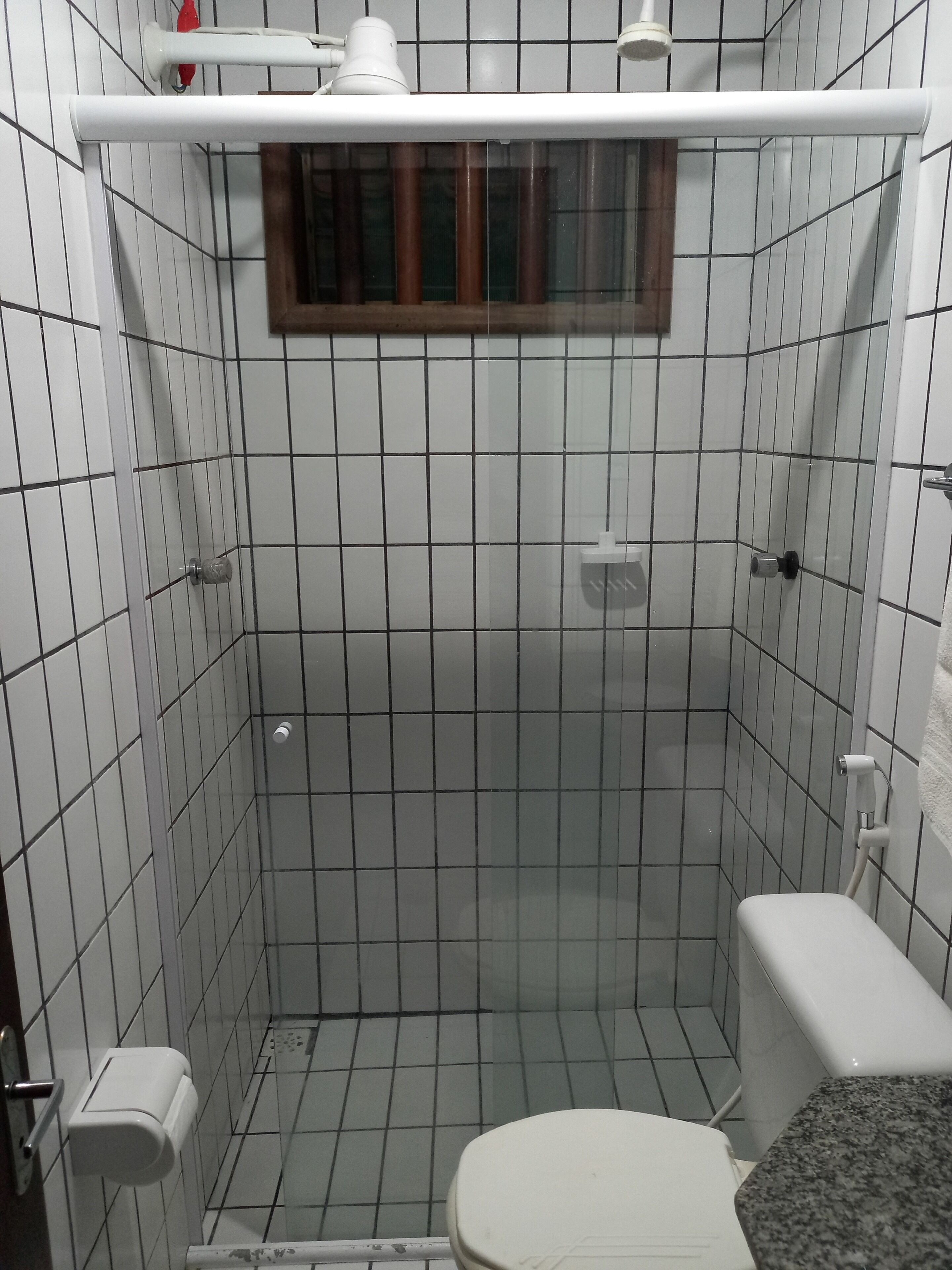Une petite salle de bain carrelée, équipée de toilettes, d’une douche et d’une fenêtre.