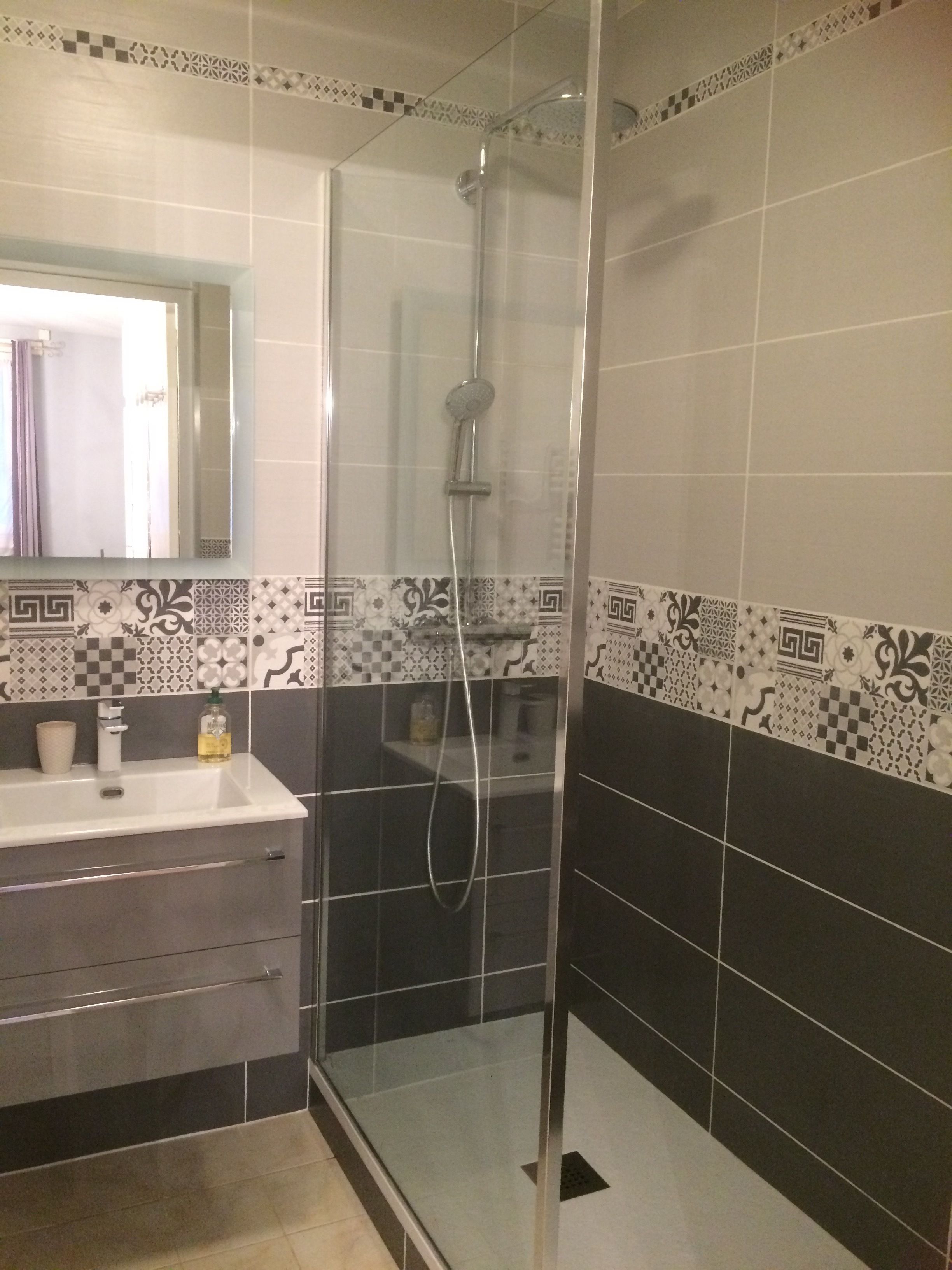 Une salle de bain avec une douche à parois de verre, un lavabo avec un miroir et des carreaux décoratifs sur les murs.