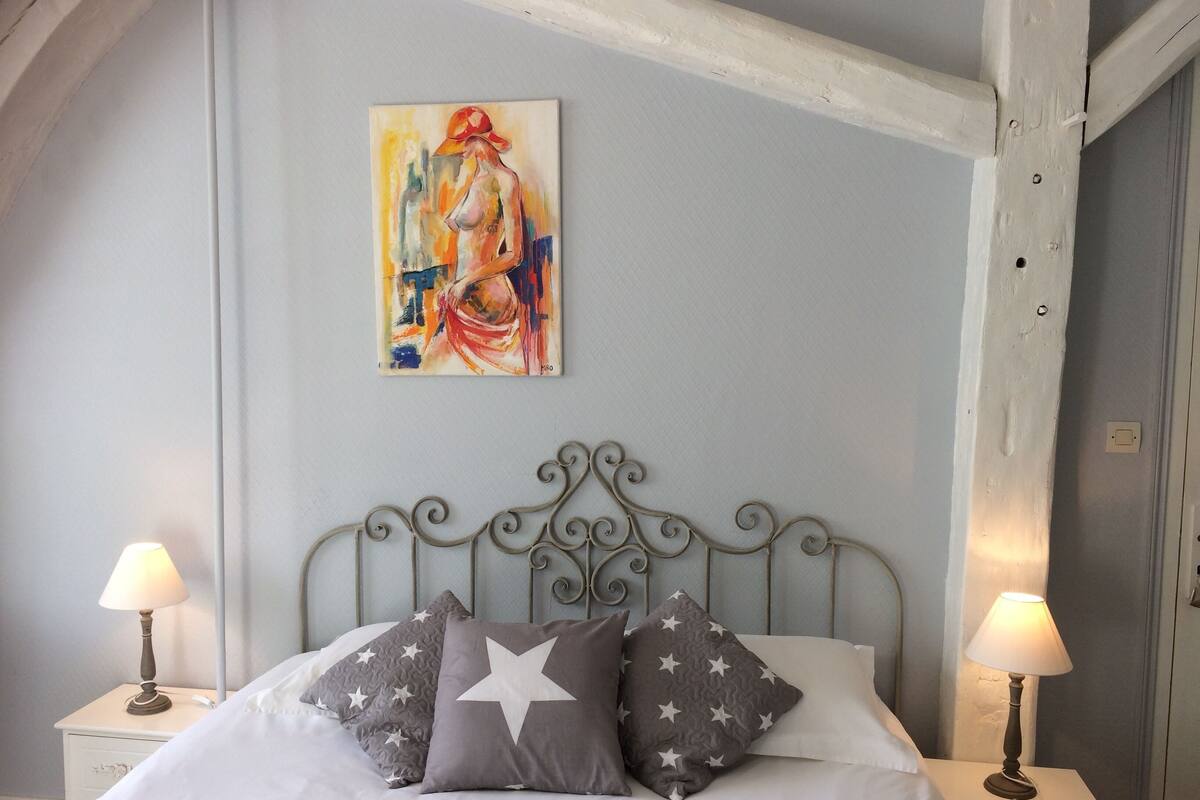 Ein Schlafzimmer mit einem Bett, zwei Nachttischlampen, einem Bild an der Wand und einem dekorativen Metall-Kopfteil.