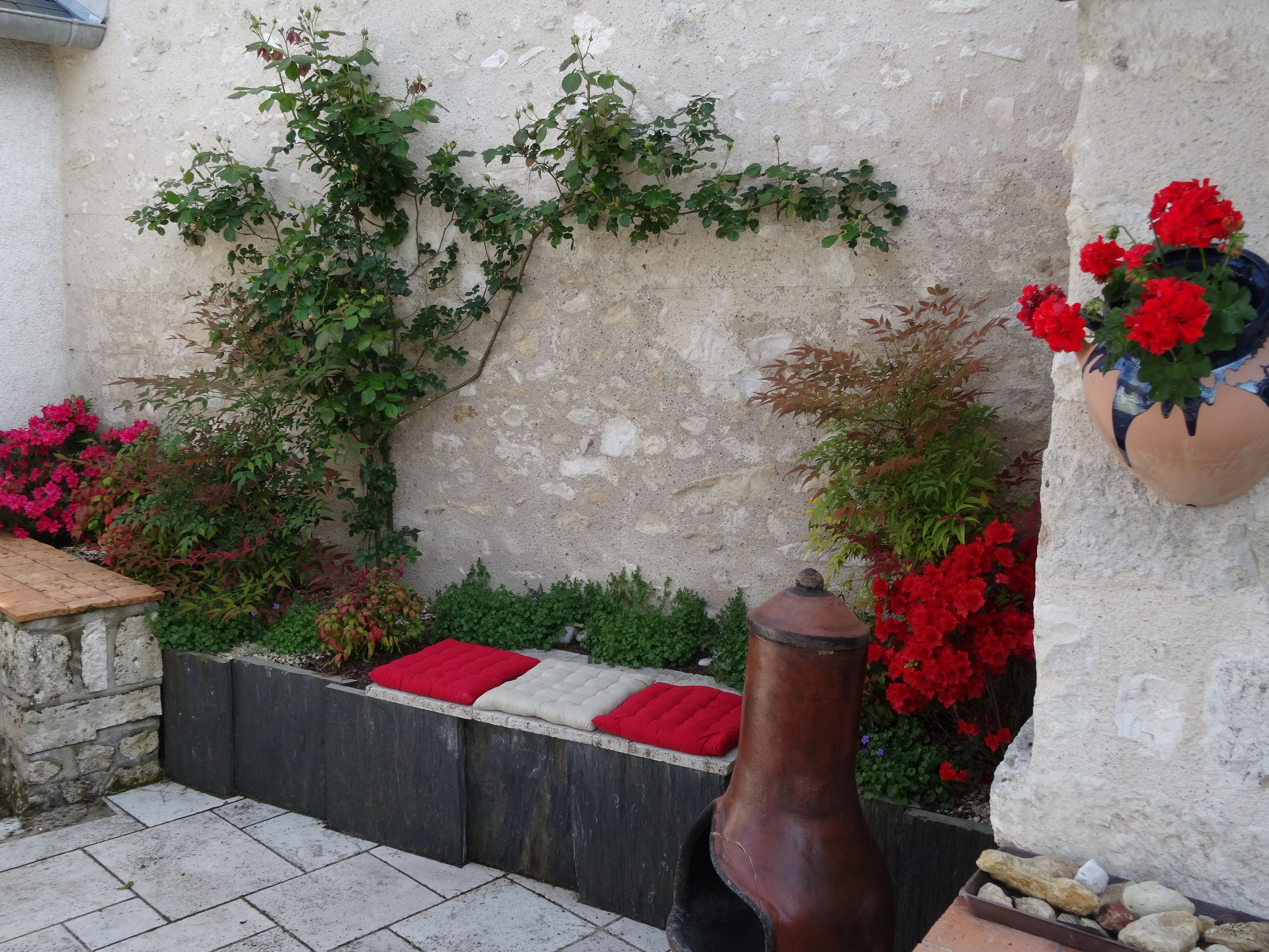 Un mur de pierre orné de plantes grimpantes et agrémenté d’un arrangement de fleurs rouges en pot.
