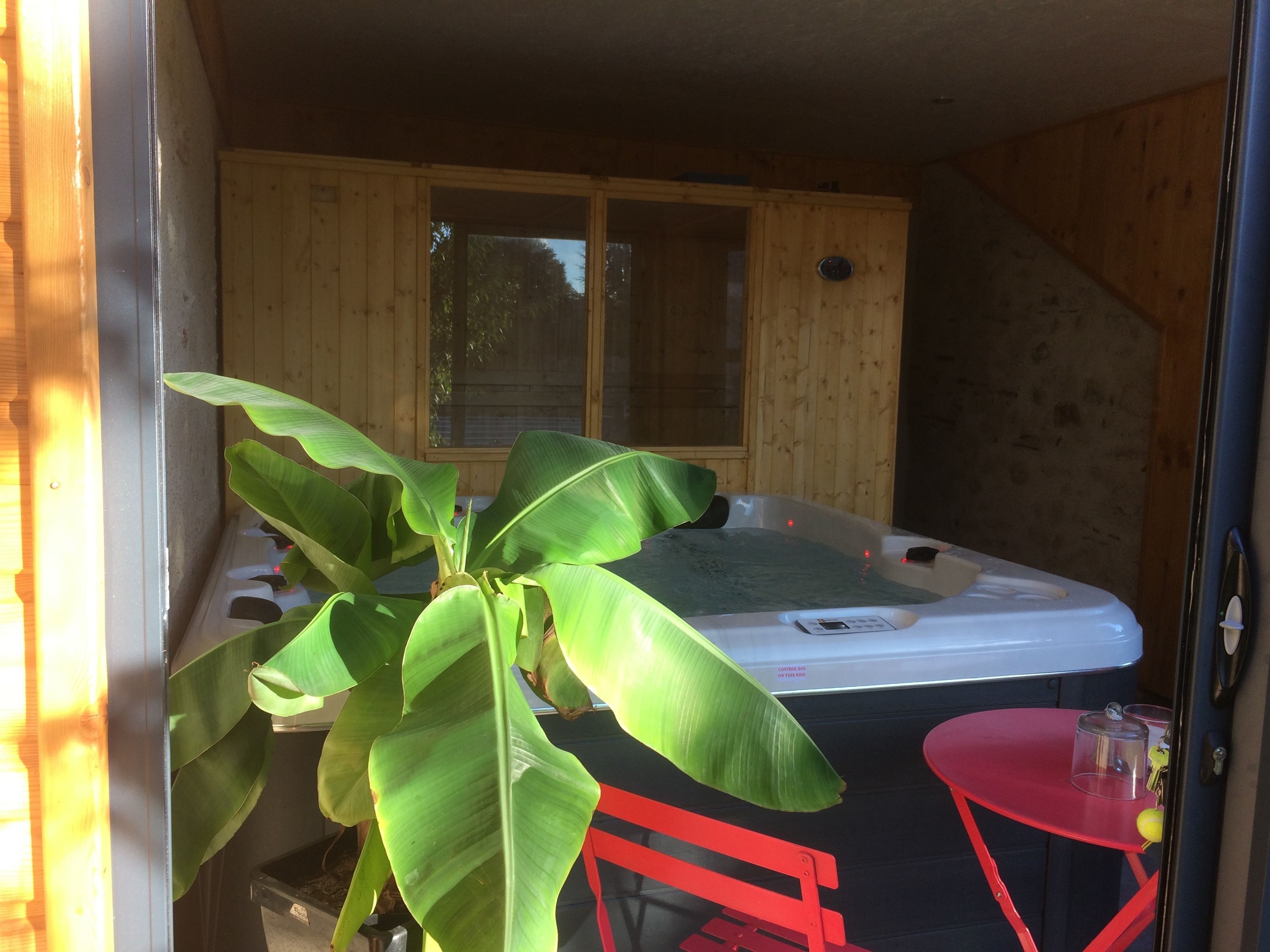 A hot tub in a wooden cabin with a red chair and a small table.