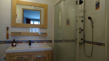 A bathroom with a glass-enclosed shower, a wooden vanity, a mirror, and a tiled backsplash.