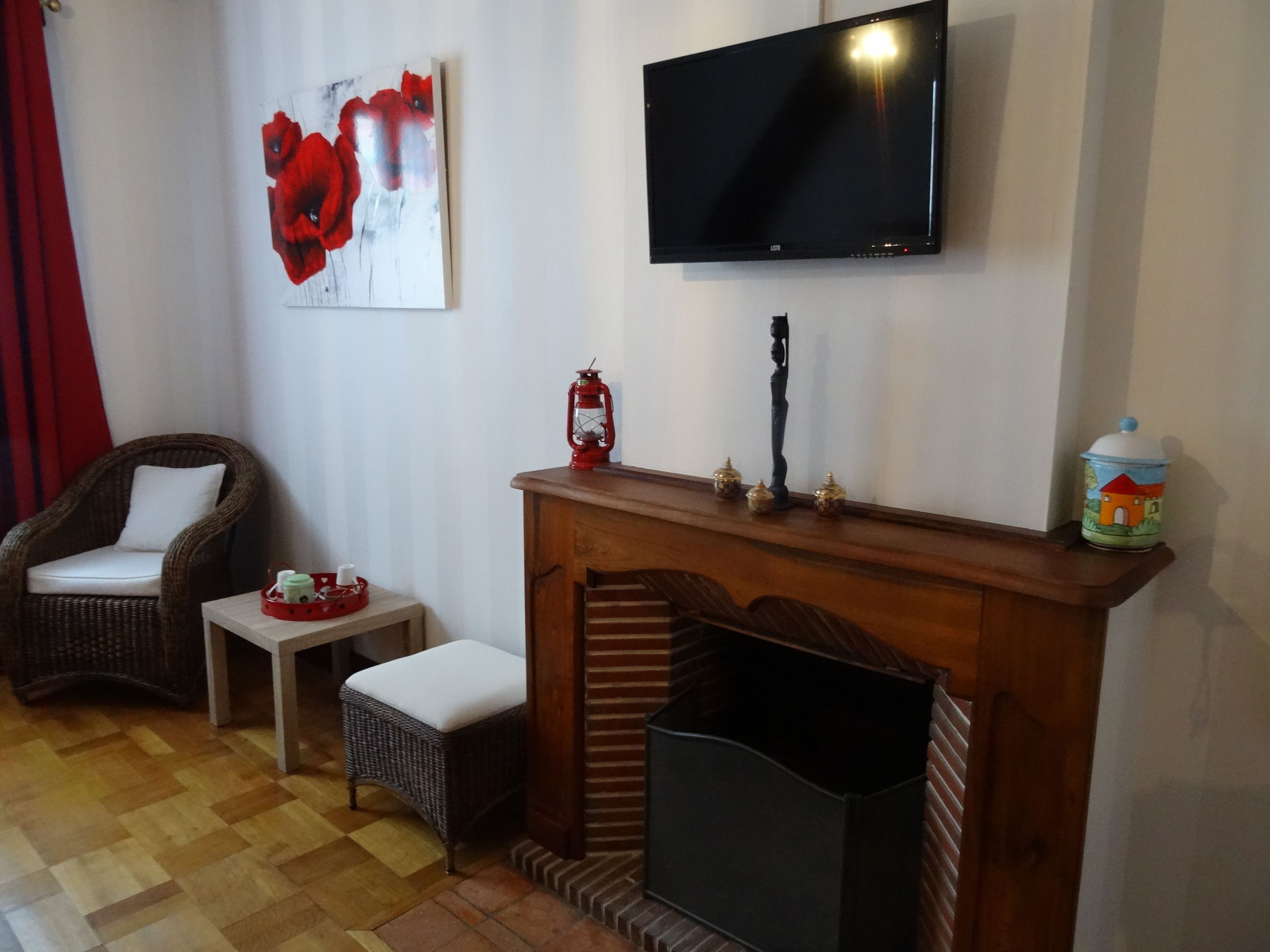 A living room with a fireplace, a television mounted on the wall, a wicker chair, a small table, and a red lantern.