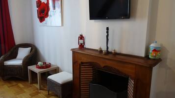A living room with a fireplace, a television mounted on the wall, a wicker chair, a small table, and a red lantern.