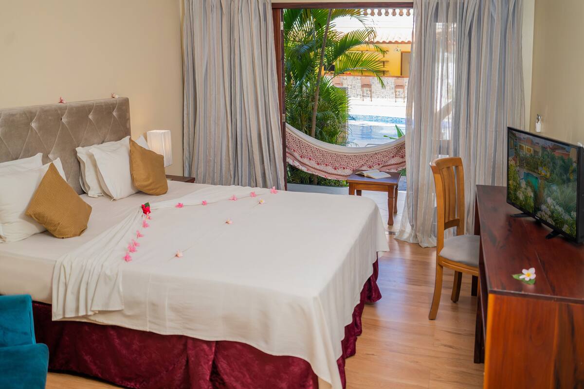 Une chambre d’hôtel avec un lit, un bureau, une chaise et une vue sur une piscine et des palmiers.