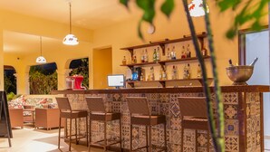 A bar area with wicker chairs, a tiled backsplash, and shelves with bottles. - Hotel Villa Beija Flor (Jijoca de Jericoacoara)