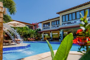 Una piscina con fuente, sillas de descanso y un área de patio techada.