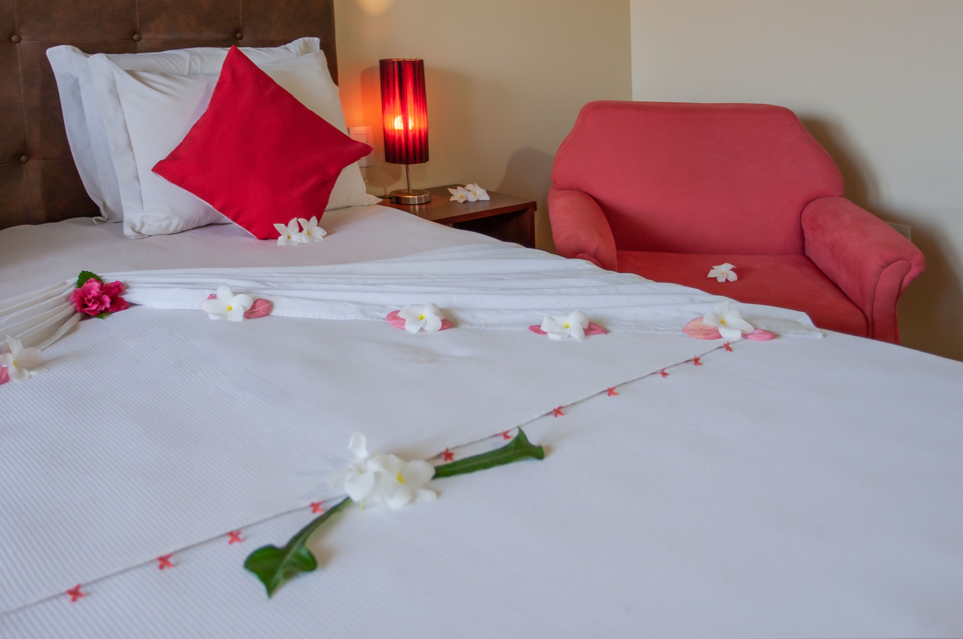 Un lit bien fait, avec du linge de lit blanc, un coussin rouge et des décorations florales.
