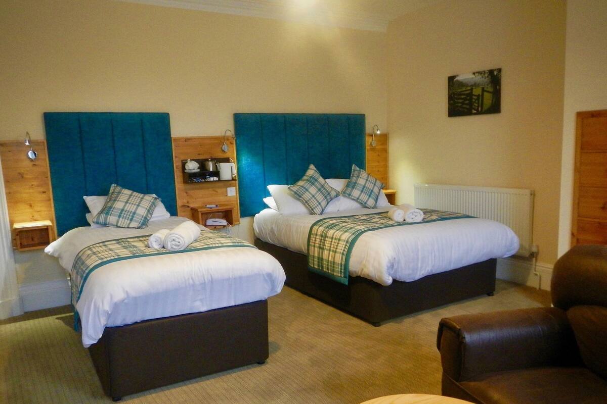 A hotel room with two beds, each with a headboard, a bedside table, and a lamp. There is a wooden chair and a round wooden table in the room.