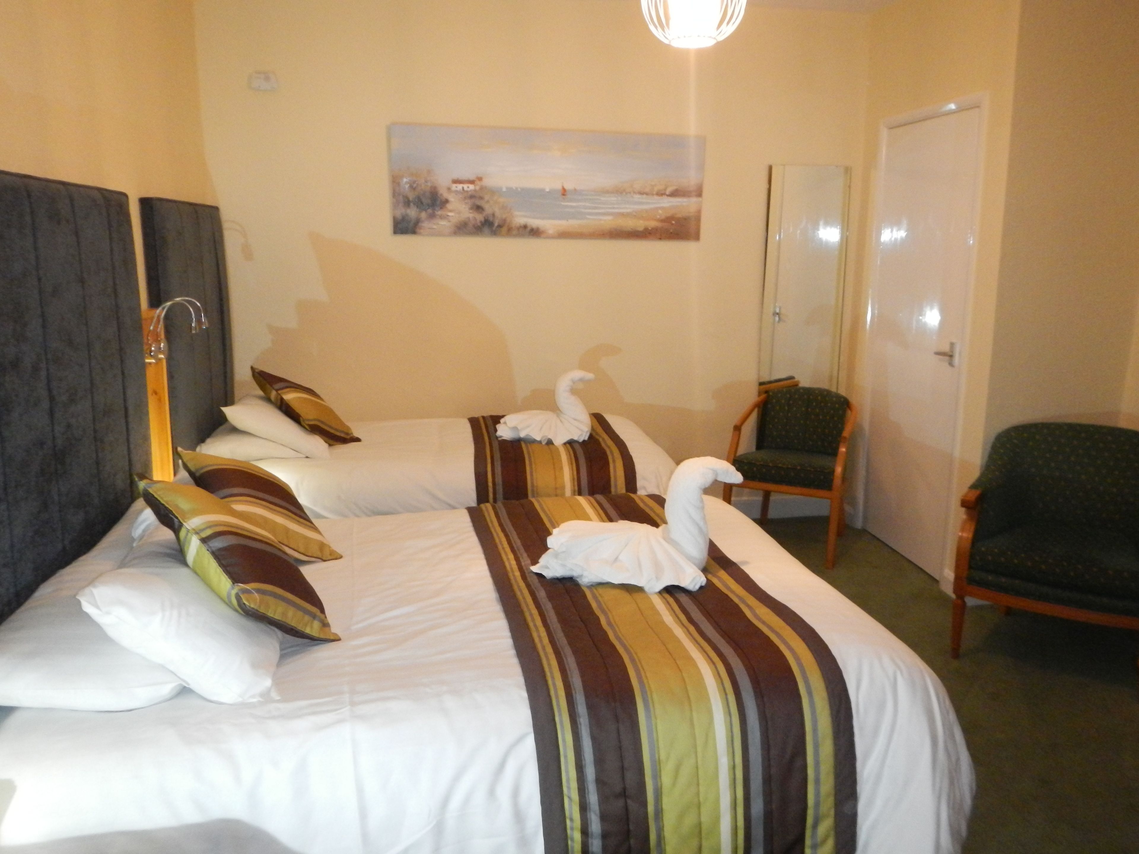 A hotel room with two beds, a painting on the wall, a chair, and a door.