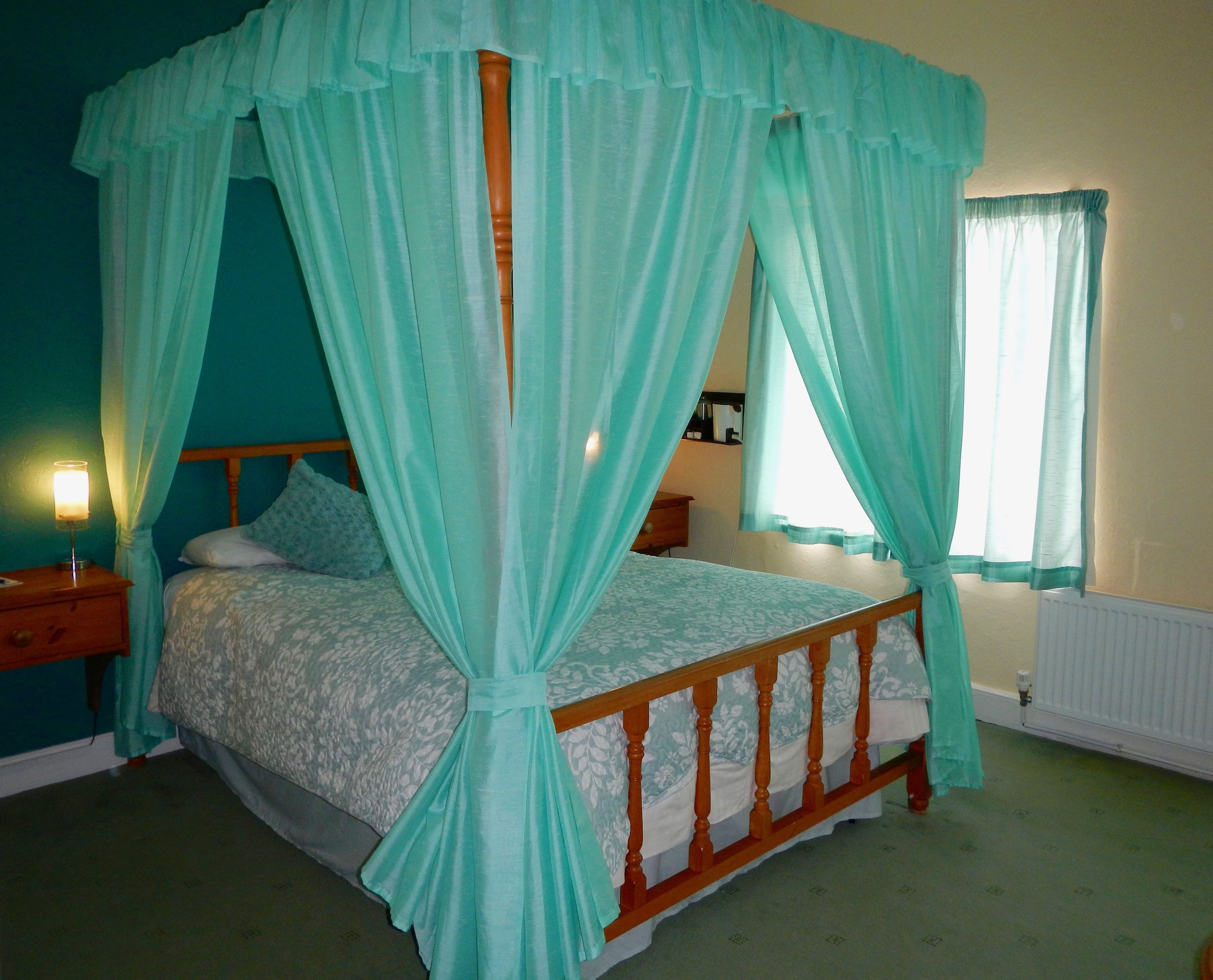 A four-poster canopy bed with a wooden frame and a light blue bedspread.