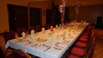 A long banquet table set with silverware, plates, and glassware, surrounded by red upholstered chairs.