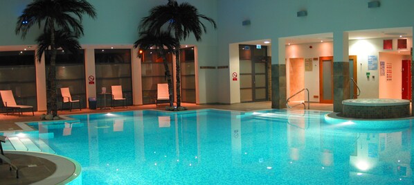 An indoor swimming pool with clear water, lounge chairs, and palm trees. - The Burton Hotel and Cloud Nine (Kington)