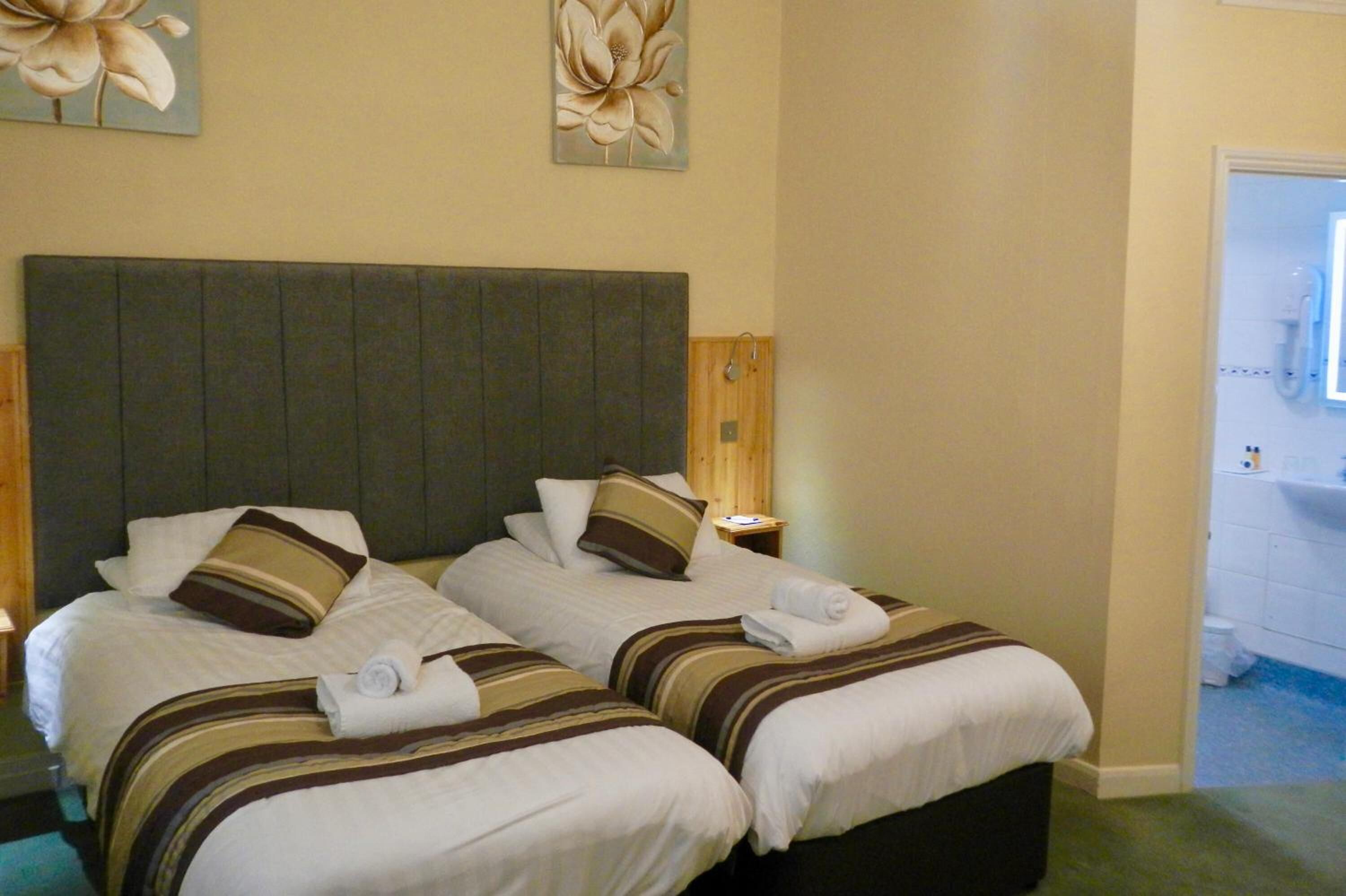 A hotel room with two beds, each with striped bedding and pillows. There are wall-mounted lamps and a wooden nightstand with a phone.