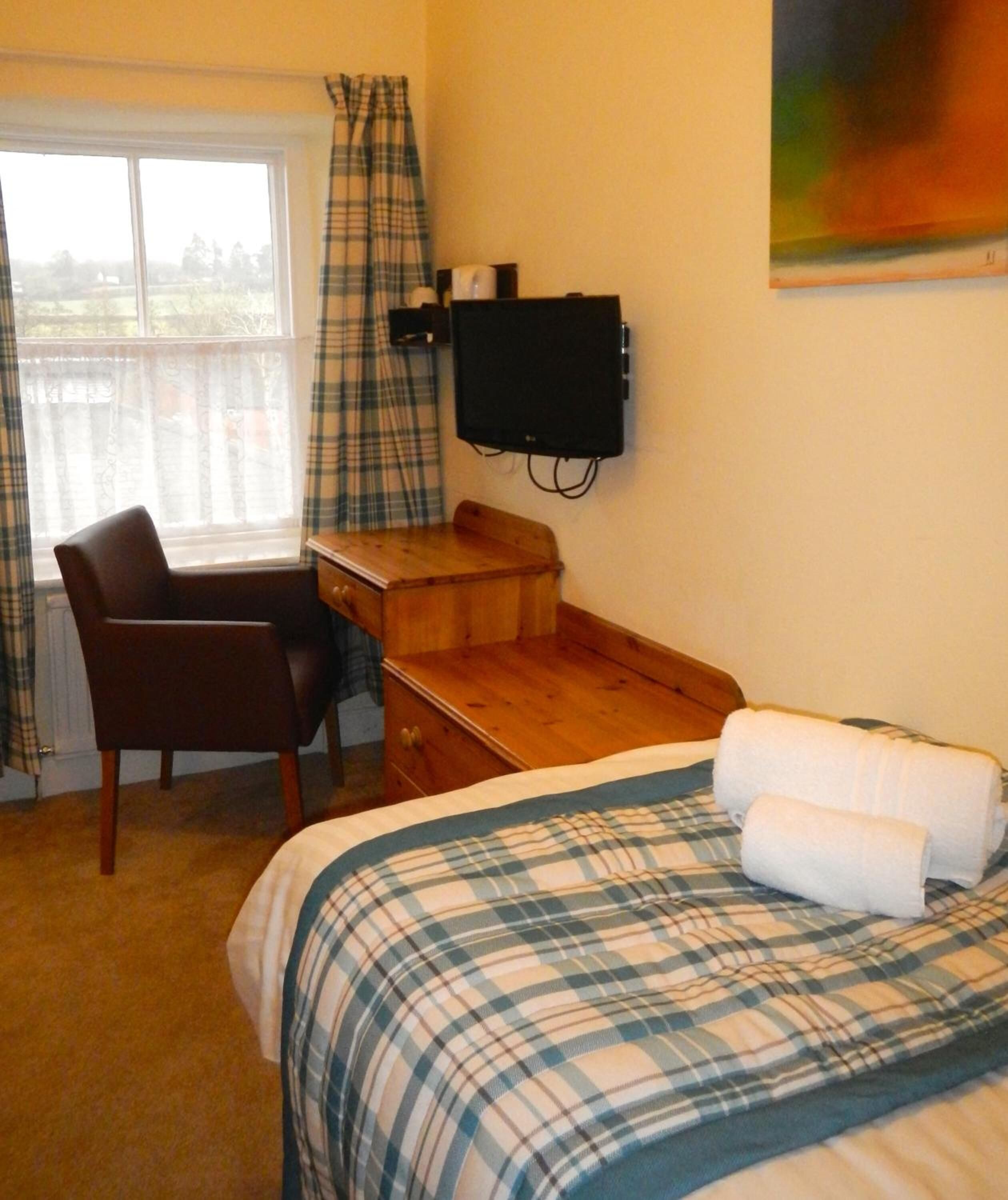 A bedroom with a bed, a desk, a chair, and a television.