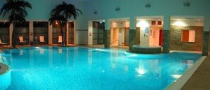 Una piscina con sillas de descanso y palmeras, rodeada de muros con puertas y ventanas.