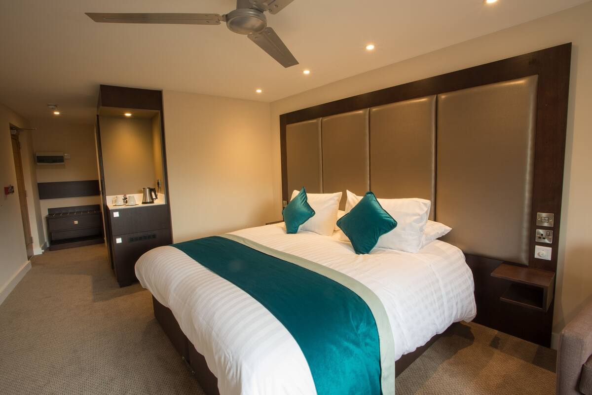 A hotel room with a large bed, a ceiling fan, a bedside table, and a nightstand.