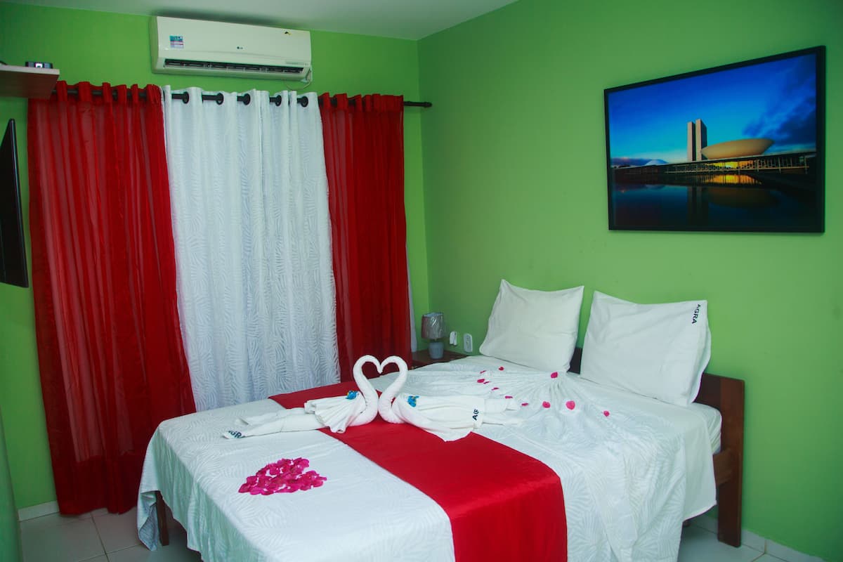 A hotel room with a bed, red and white curtains, a painting of a bridge, and a swan decoration on the bed.