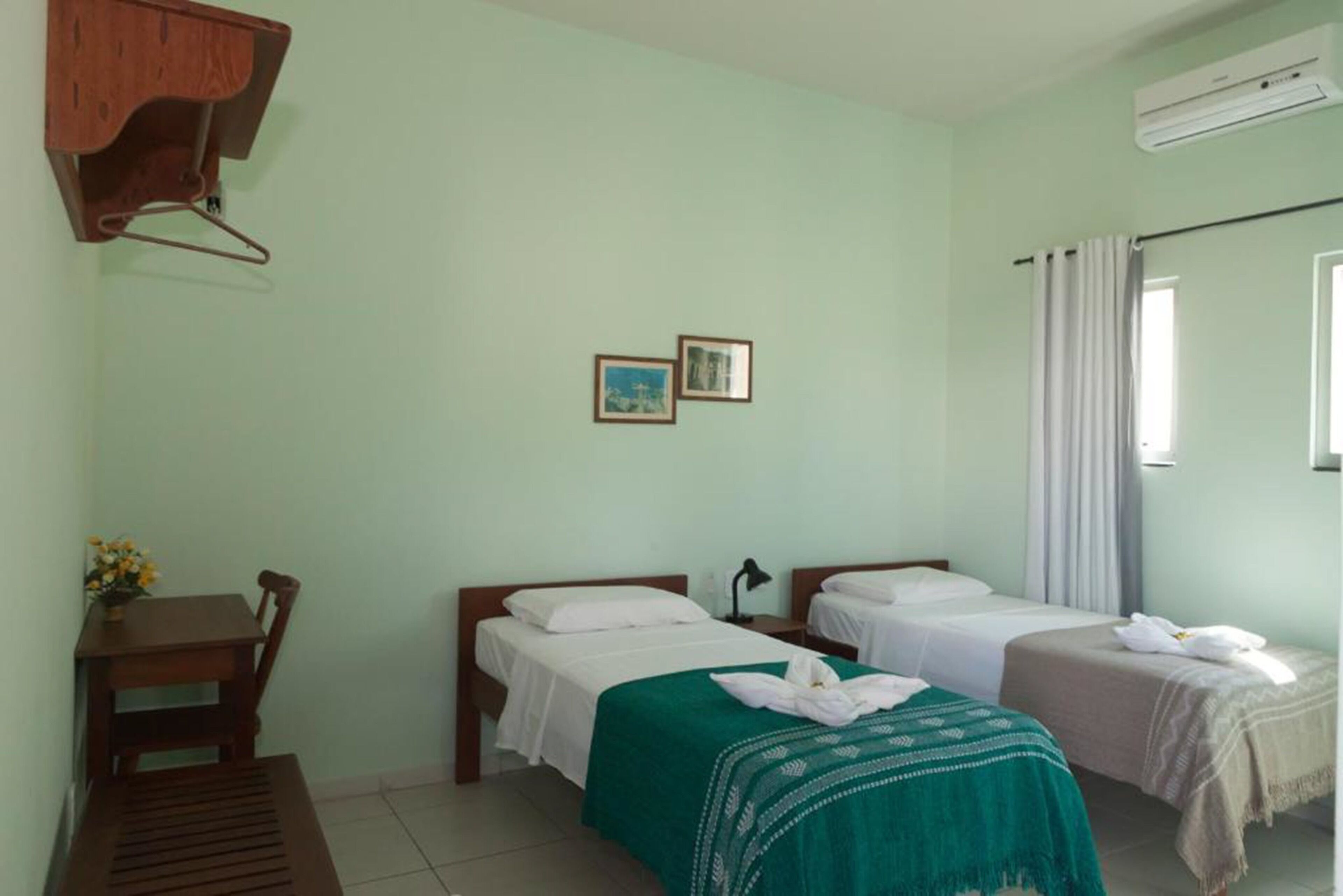 Una habitación con dos camas, un escritorio y una silla. Hay dos cuadros en la pared.