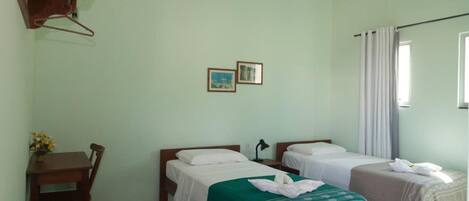 Una habitación con dos camas, un escritorio y una silla. Hay dos cuadros en la pared.