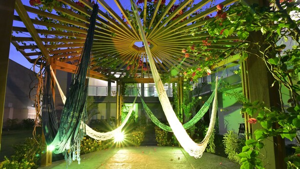 Un jardín con un porche de madera, hamacas verdes y blancas, y un sendero bien iluminado.