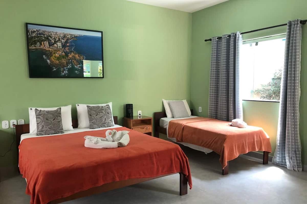A hotel room with two beds, green walls, a painting of a coastal city, and a window with curtains.
