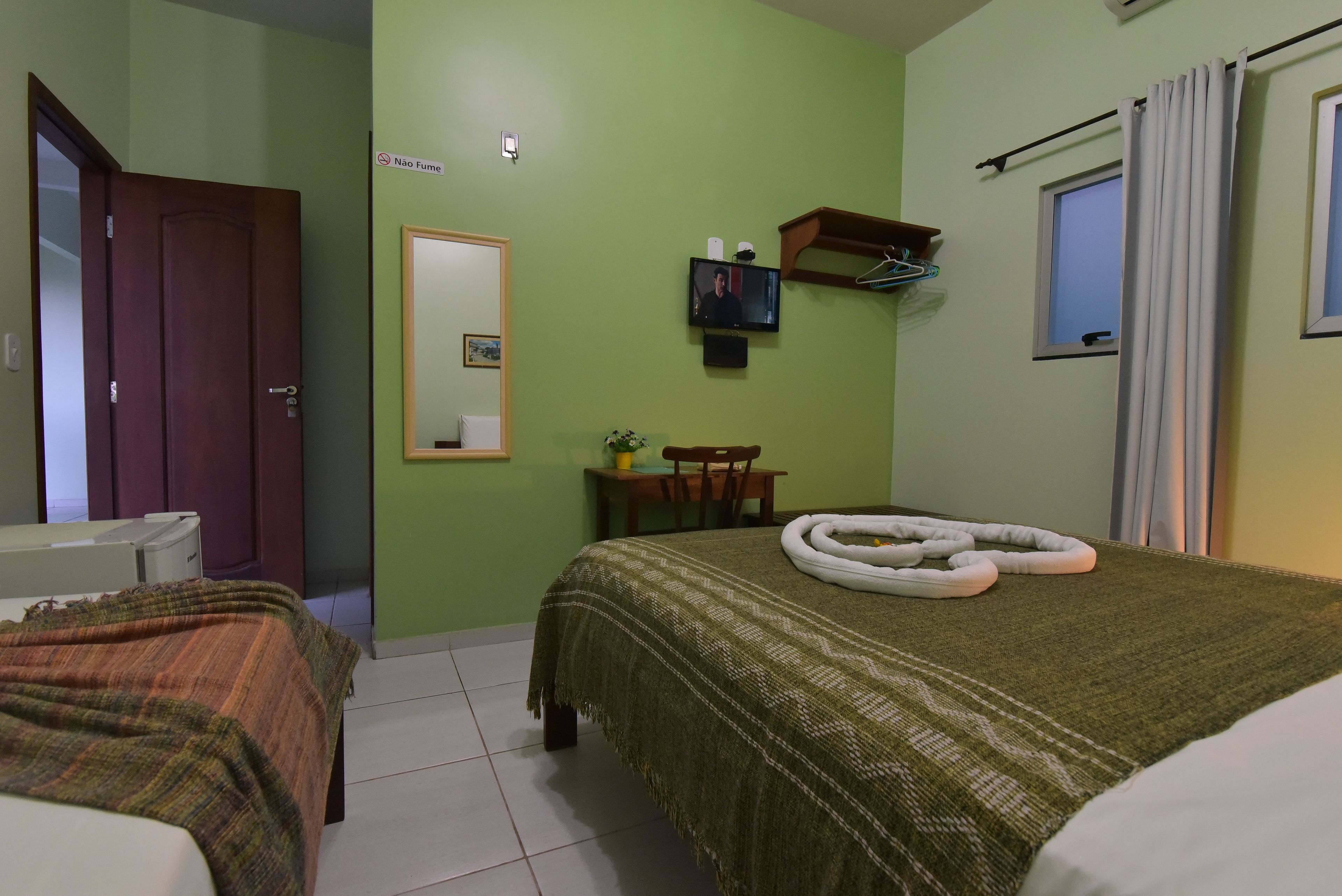 A hotel room with a bed, a chair, a small table, a TV, and a window with curtains.