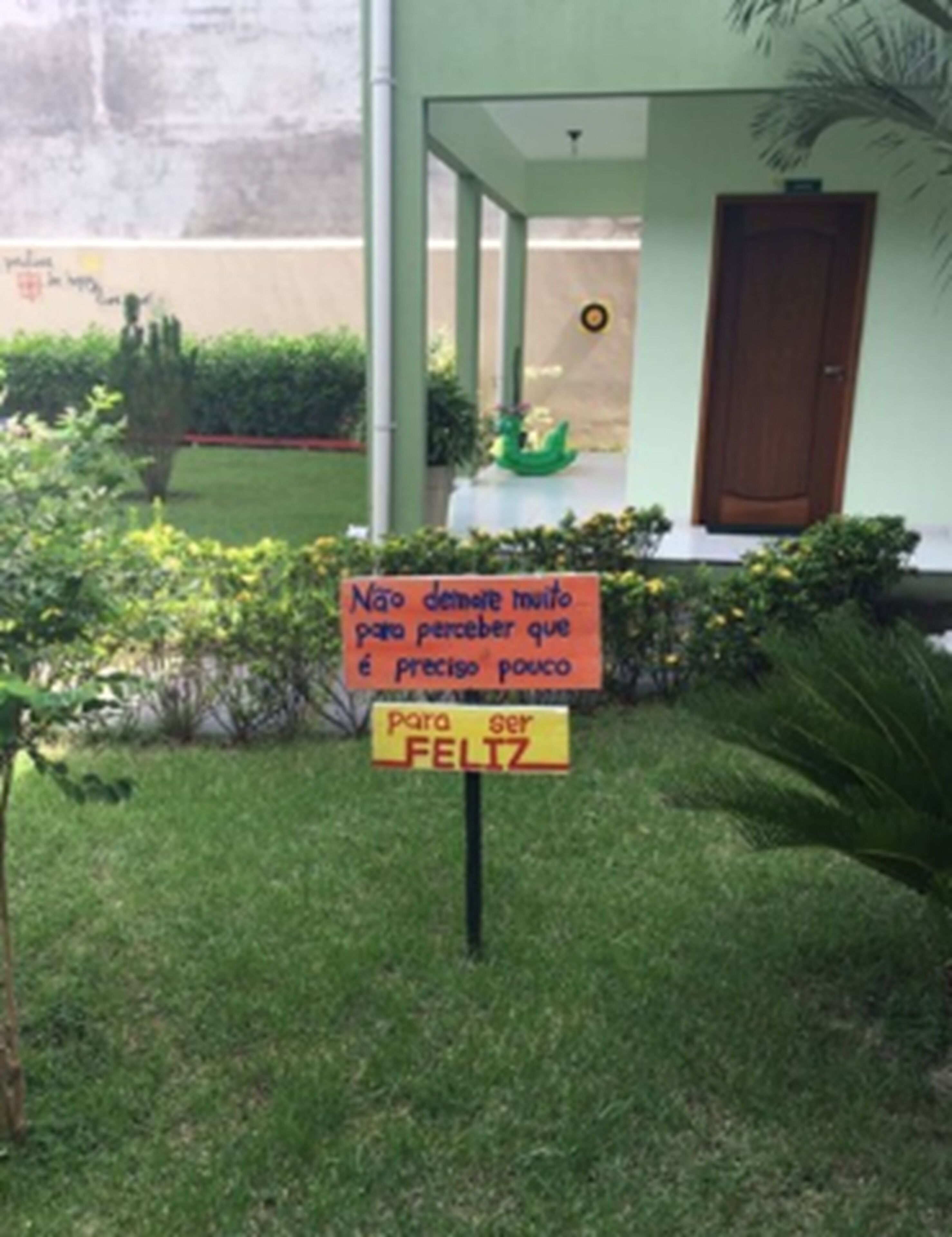 Un cartel frente a un edificio con puerta verde y un pequeño jardín.