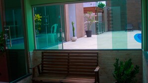 Un balcón con banca de madera, plantas en macetas y vista a una piscina.