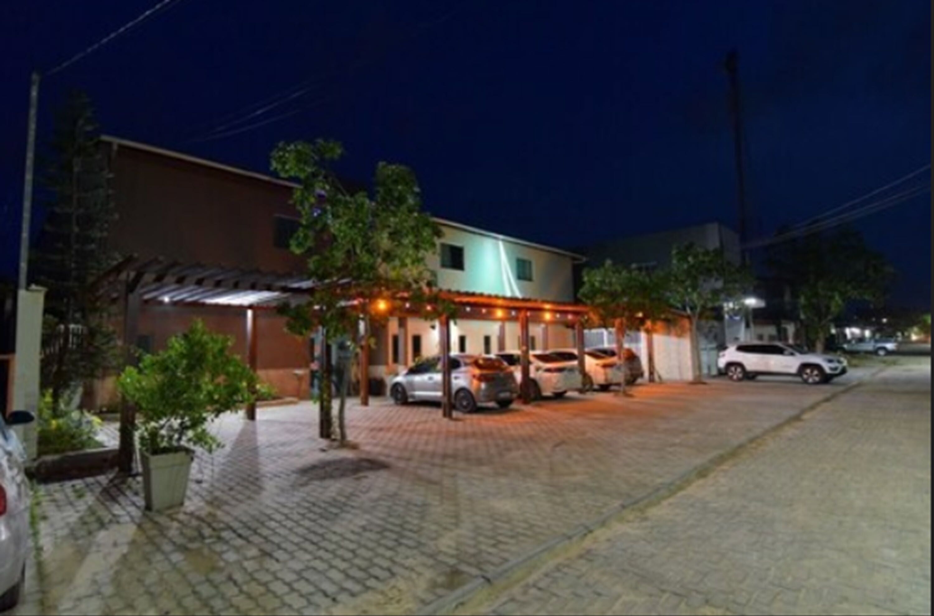 A building with a covered outdoor area, several parked cars, and a paved driveway.