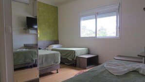 A room with two beds, a television on a shelf, and a window with blinds. - Adoro Hotel (Farroupilha)