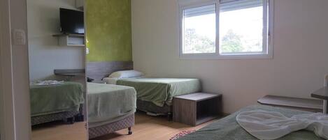 Una habitación con dos camas, un televisor sobre una estantería y una ventana con persianas.