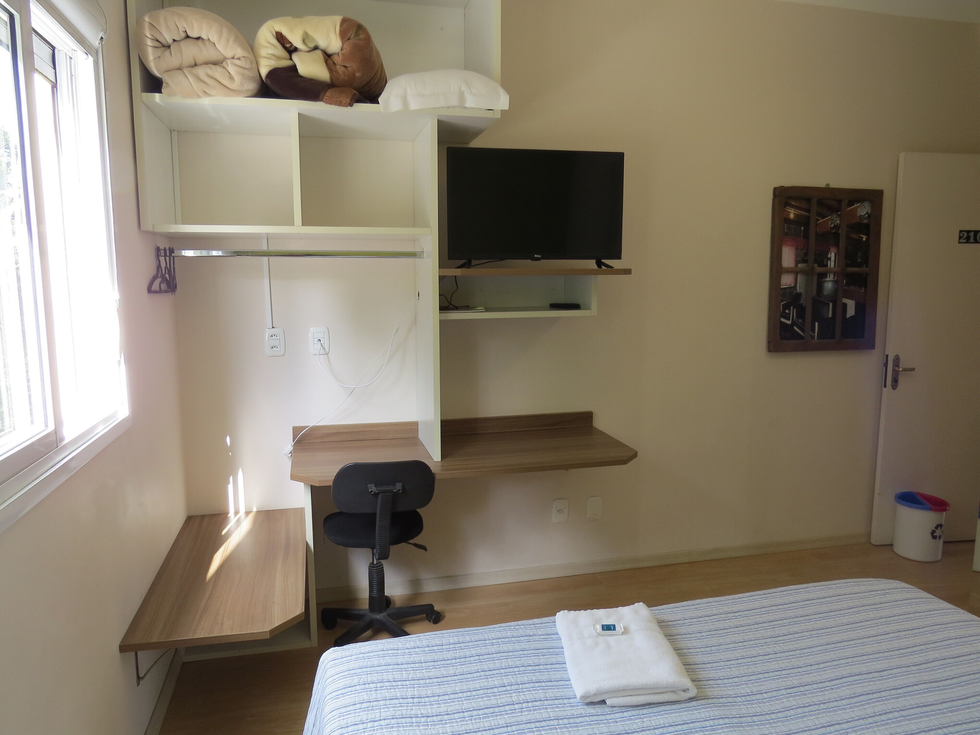 A bedroom with a bed, a desk, a chair, a television, and a wardrobe.