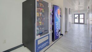 Un pasillo con máquinas expendedoras, incluyendo una de Pepsi y una de Coca-Cola, y una puerta al final.