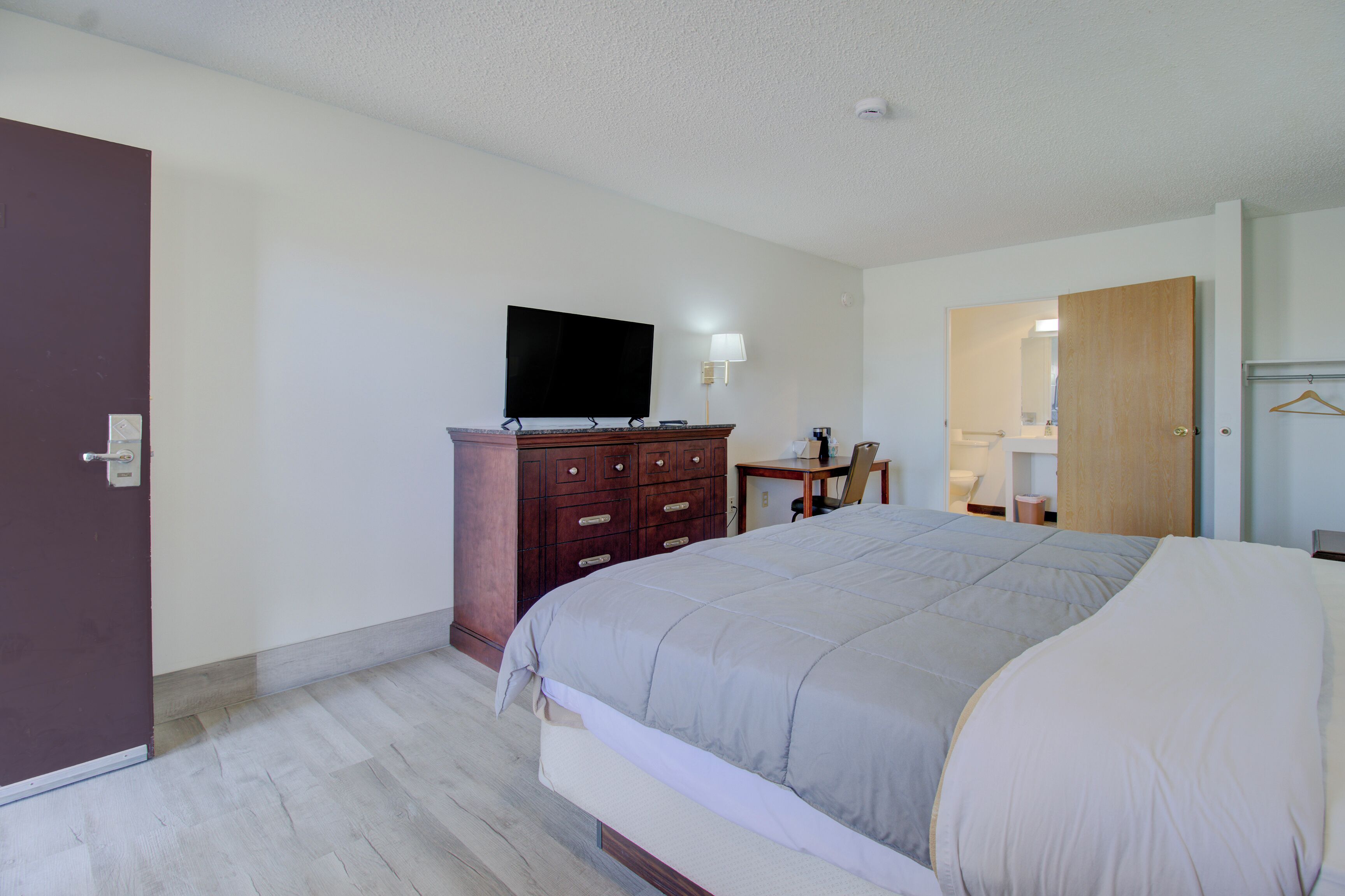 A hotel room with a bed, a dresser, a television, a desk with a chair, and a mirror.