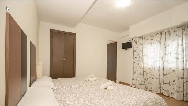 A bedroom with a bed, a wardrobe, a television, and a window with curtains. - Hostal Ávila (Zaragoza)