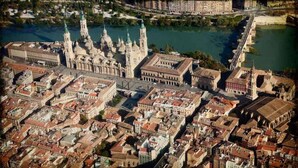 An aerial view of a historic city with prominent architecture, including a large cathedral with multiple spires and a river running through the city. - Hostal Ávila (Zaragoza)