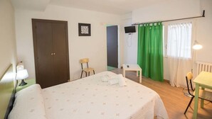 A bedroom with a bed, a desk, a chair, a door, and a green curtain. - Hostal Ávila (Zaragoza)