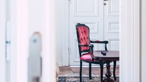 Quarto com porta branca, cadeira estofada vermelha, mesa de madeira e tapete estampado no chão.