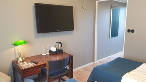 Quarto de hotel com escrivaninha, cadeira, duas camas, televisão e porta que dá para outro aposento.