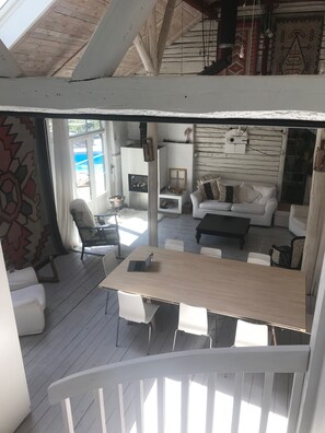 A cozy, open-plan living area with a wooden deck, a white sofa set, a dining table with chairs, and a fireplace.